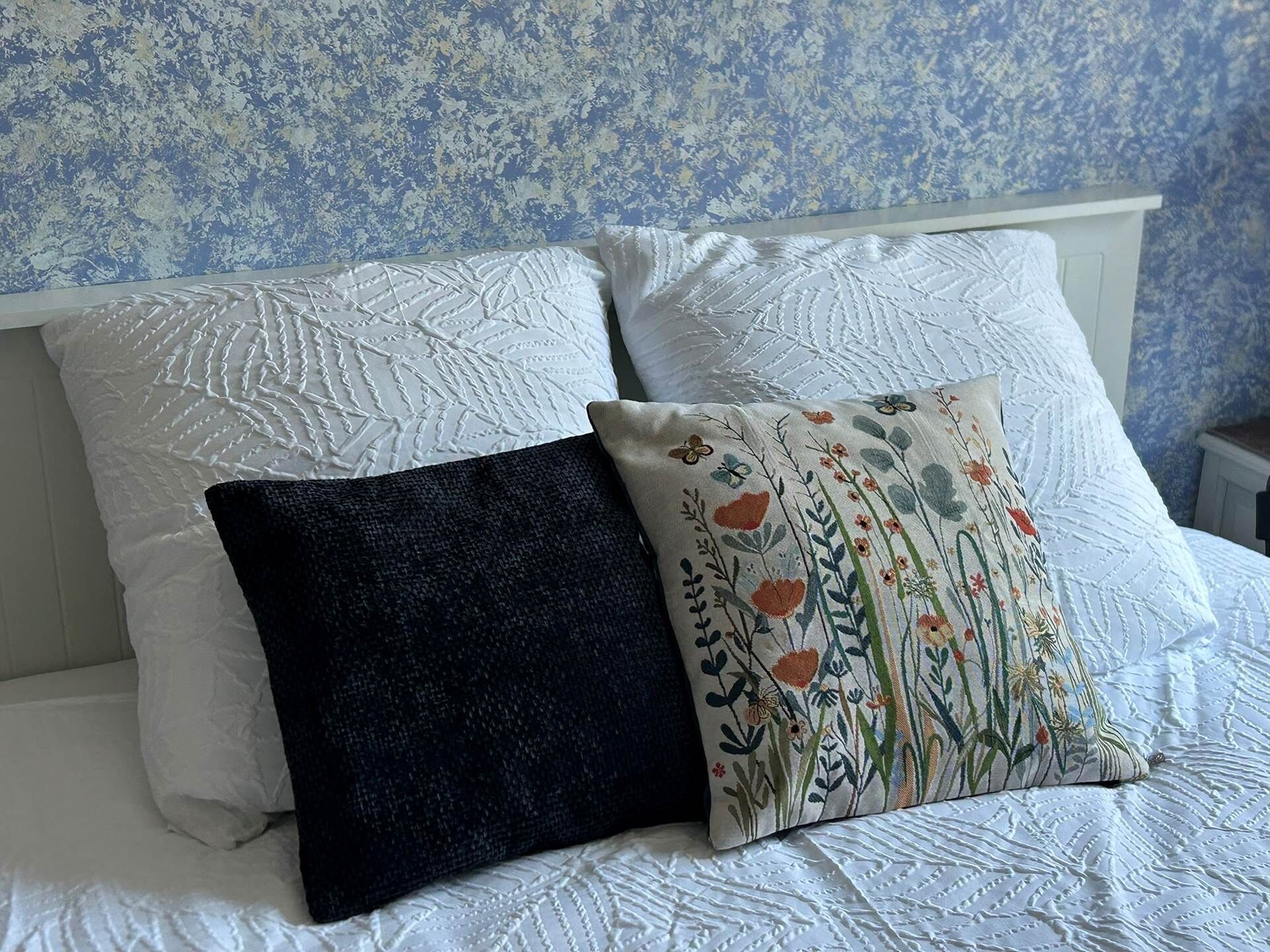 Un lit avec deux oreillers blancs et un oreiller noir orné de broderies florales.