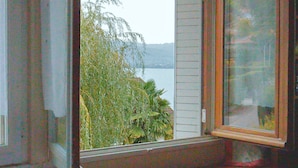 A bedroom with a large window, a bed, and a wooden dresser. - Villa Jasmin (Veyrier-du-Lac)