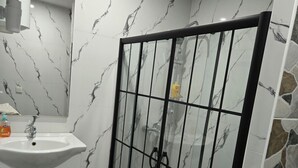 Une salle de bain avec un pare-baignoire en marbre, un lavabo, une douche à parois de verre et un porte-serviettes.