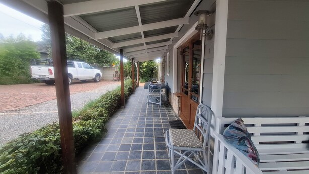 A covered outdoor area with a tiled floor, a white pickup truck parked on the street, and a row of chairs and a bench along the wall. - Gables B&B Guesthouse (George)