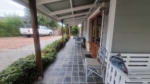 A covered porch with a tiled floor, two metal chairs, a white bench, and a white truck parked outside. - Gables B&B Guesthouse (George)