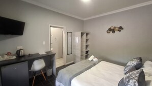 A hotel room with a bed, a desk, a chair, a wardrobe, and a television. - Gables B&B Guesthouse (George)