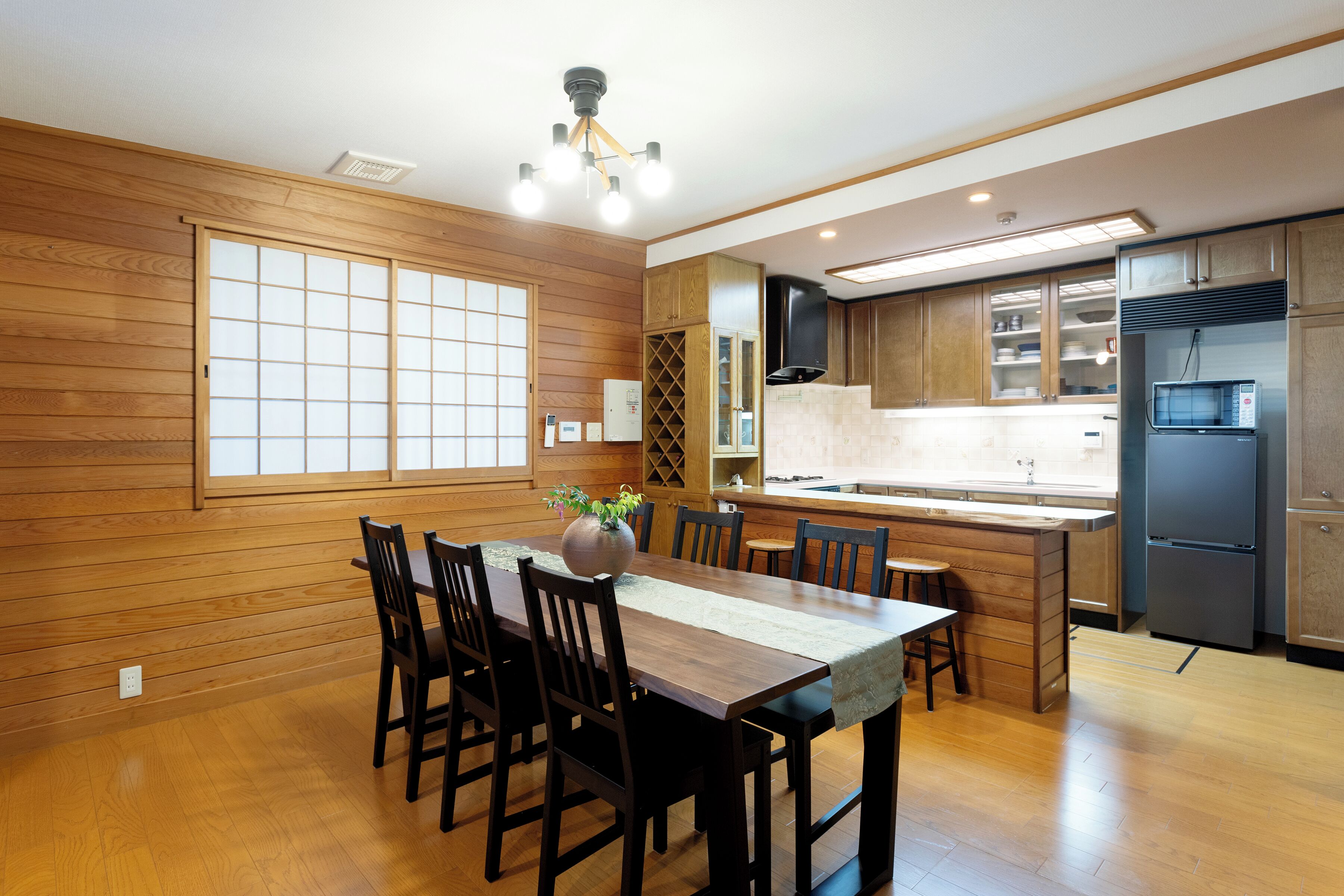 Une cuisine moderne avec des meubles en bois, une table à manger avec des chaises et un îlot central intégré avec des tabourets.