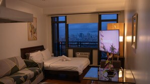 Ein Hotelzimmer mit Bett, einer Couch, einem Fernseher und Blick auf die Stadt.
