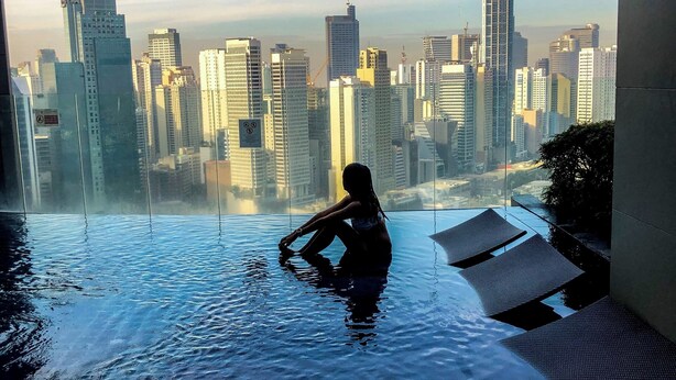 Eine Person entspannt in einem Infinity-Pool mit Blick auf die Stadt.