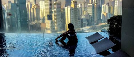 A person sitting in an infinity pool with a cityscape view.