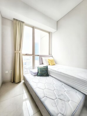Une chambre moderne avec une grande fenêtre, un lit doté d’un matelas blanc et d’un oreiller vert.