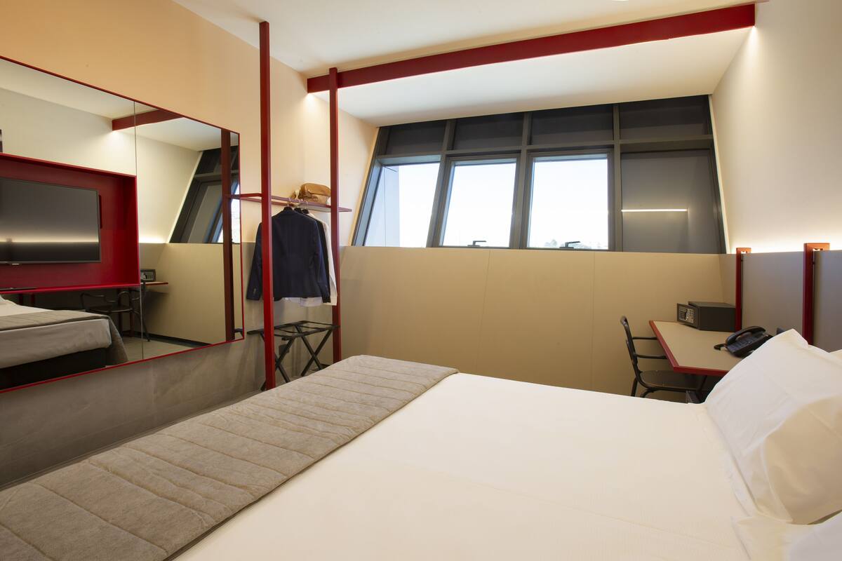 A hotel room with a bed, a desk, a chair, a TV, and a window.