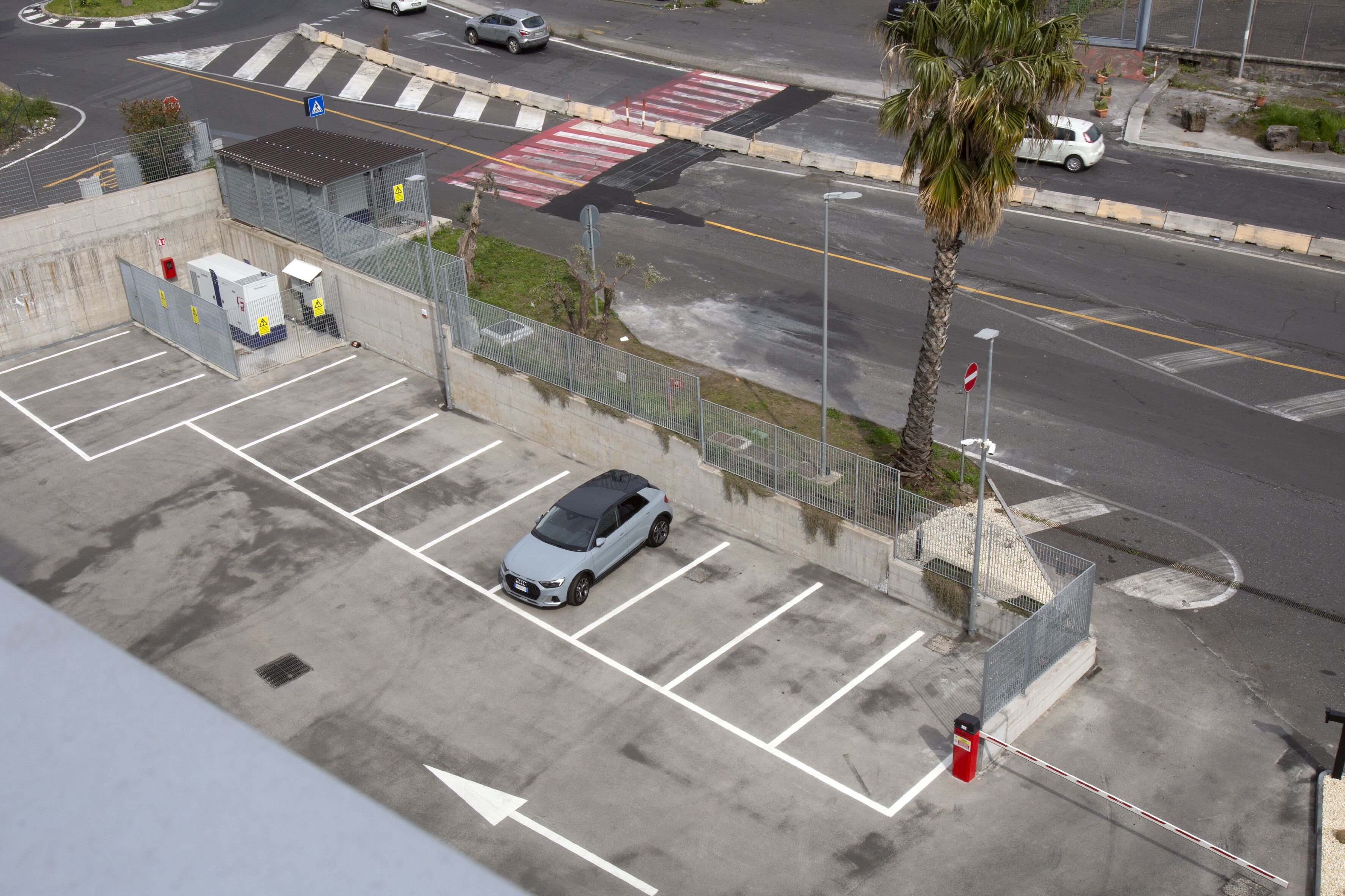 An aerial view of a parking lot with a car, a palm tree, and a road intersection.