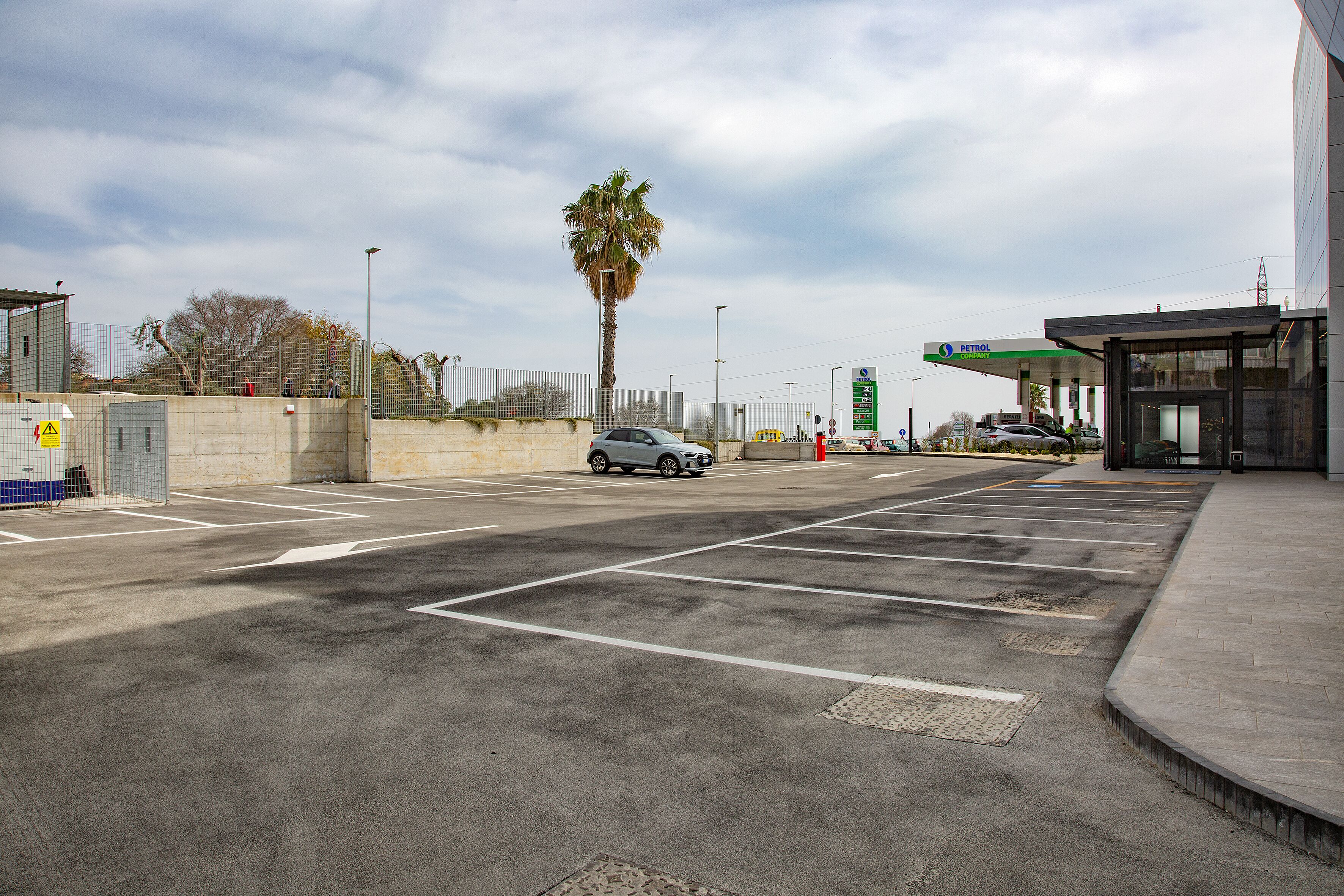 Un estacionamiento con una palmera, una gasolinera y un edificio de fachada curva.