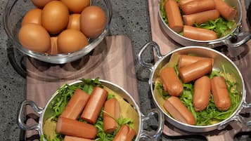 Uma bancada de cozinha com três tigelas contendo ovos e cachorros-quentes sobre uma tábua de corte.
