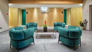 Eine Lobby mit türkisfarbenen Sesseln, einem Couchtisch, einer Topfpflanze und einem Schild mit der Aufschrift 'CUBIKinn DESIGN ROOMS'.