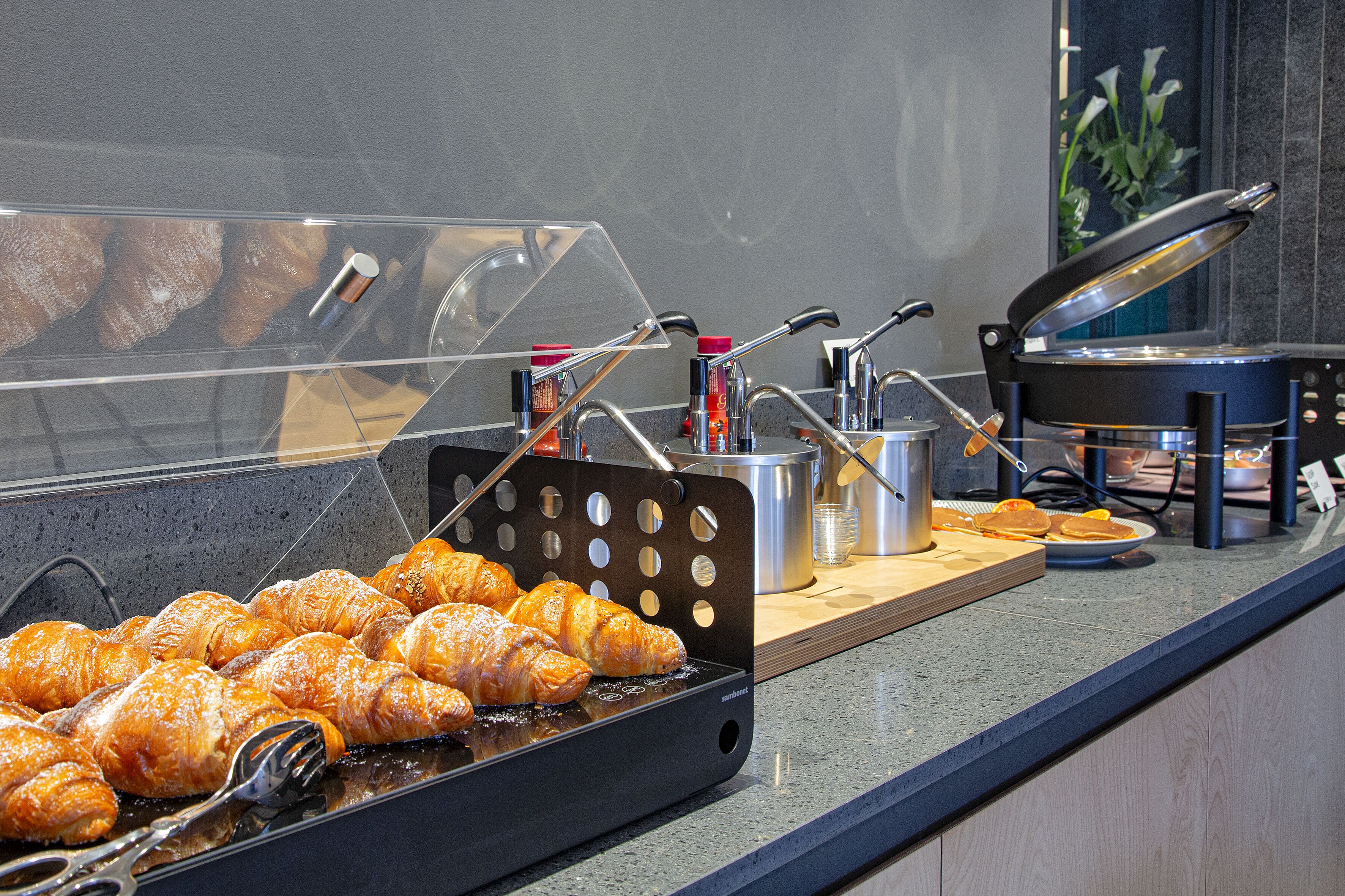 A buffet counter with a glass display case containing pastries, a hot grill, and various kitchen utensils.