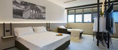 Una habitación de hotel moderna con una cama grande, un sofá pequeño, un televisor y una ventana con vista a la ciudad.