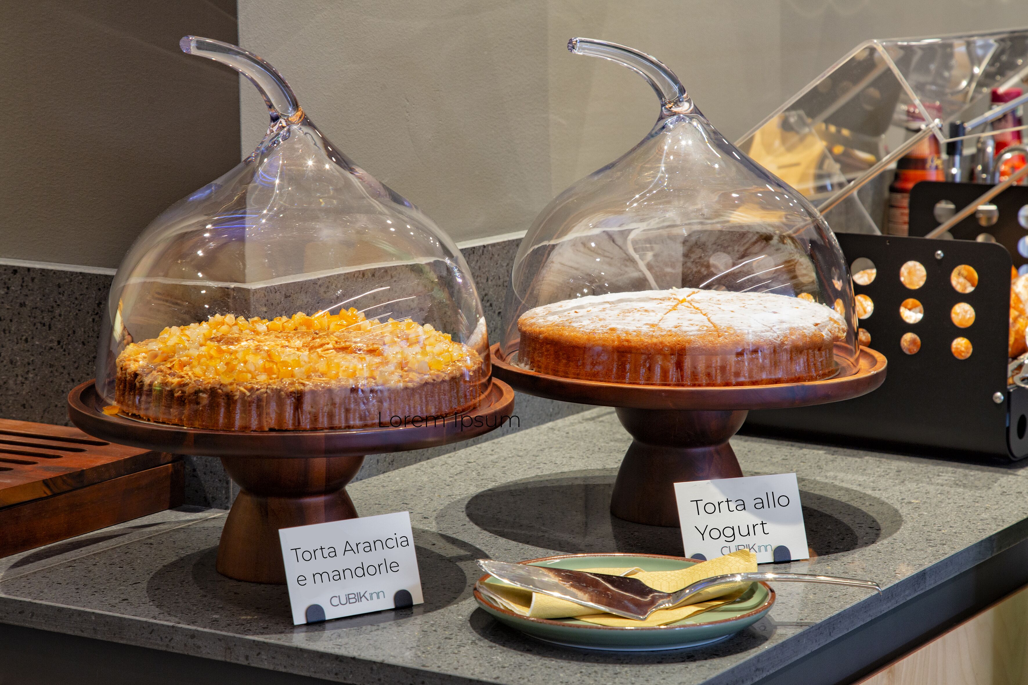 Dues vitrines per a postres cobertes, amb etiquetes, una safata metàl·lica i un plat amb coberts.