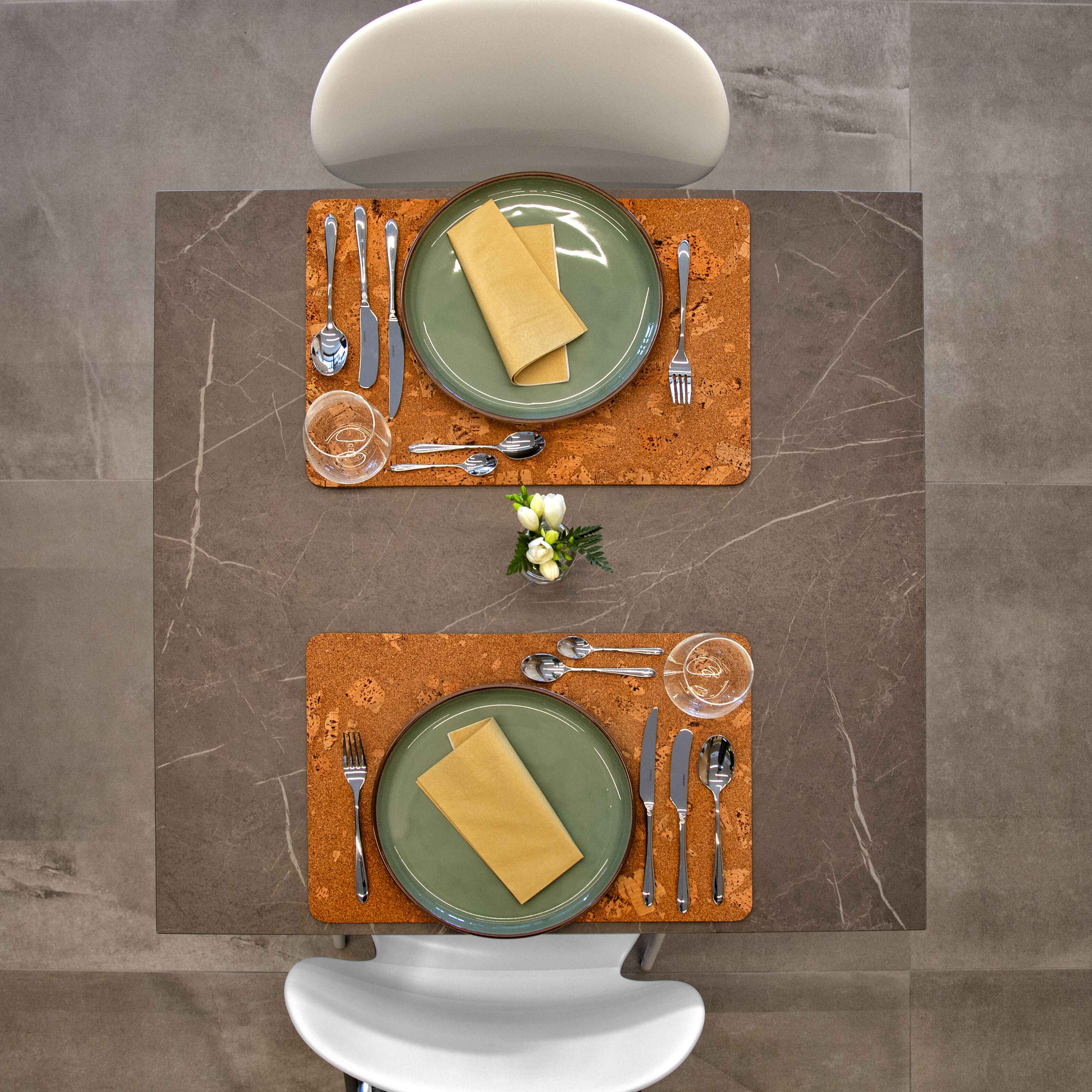 Une table à manger dressée avec de l’assiette verte, des couverts et une serviette, le tout posé sur un dessous de plat en liège.