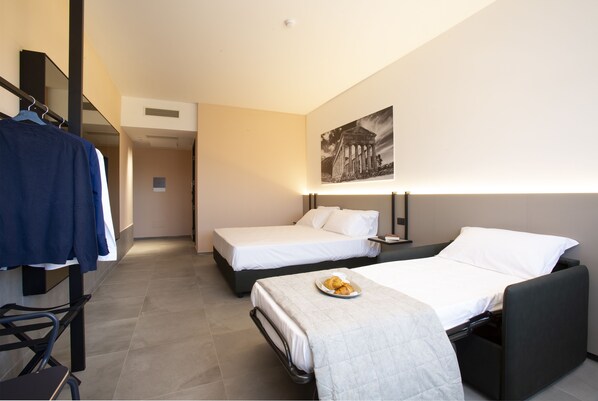 Habitación de hotel con dos camas, un escritorio y una silla. Hay un cuadro en la pared y un plato de comida sobre la cama.