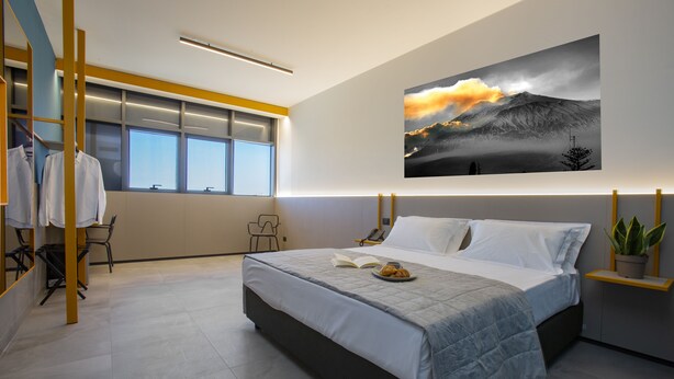 Ein modernes Schlafzimmer mit einem großen Bett, einem Fenster mit Blick, einem Bild an der Wand und einem kleinen Tisch mit einer Pflanze.