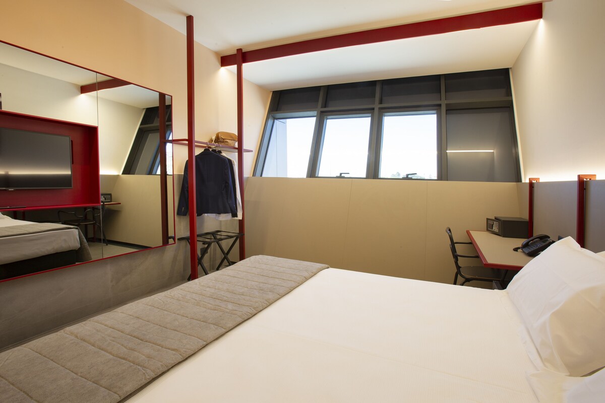 Una habitación de hotel con cama, escritorio, silla, televisión y ventana.