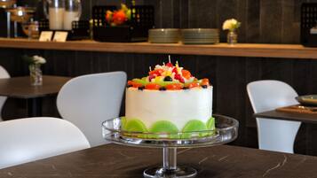 A cake on a glass stand in a dining area with chairs and a counter in the background.