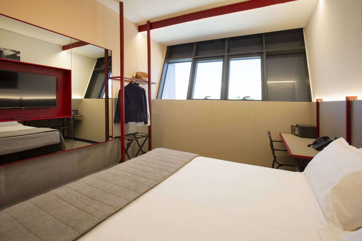 A modern hotel room with a bed, a desk, a chair, a TV, and a window with a view.