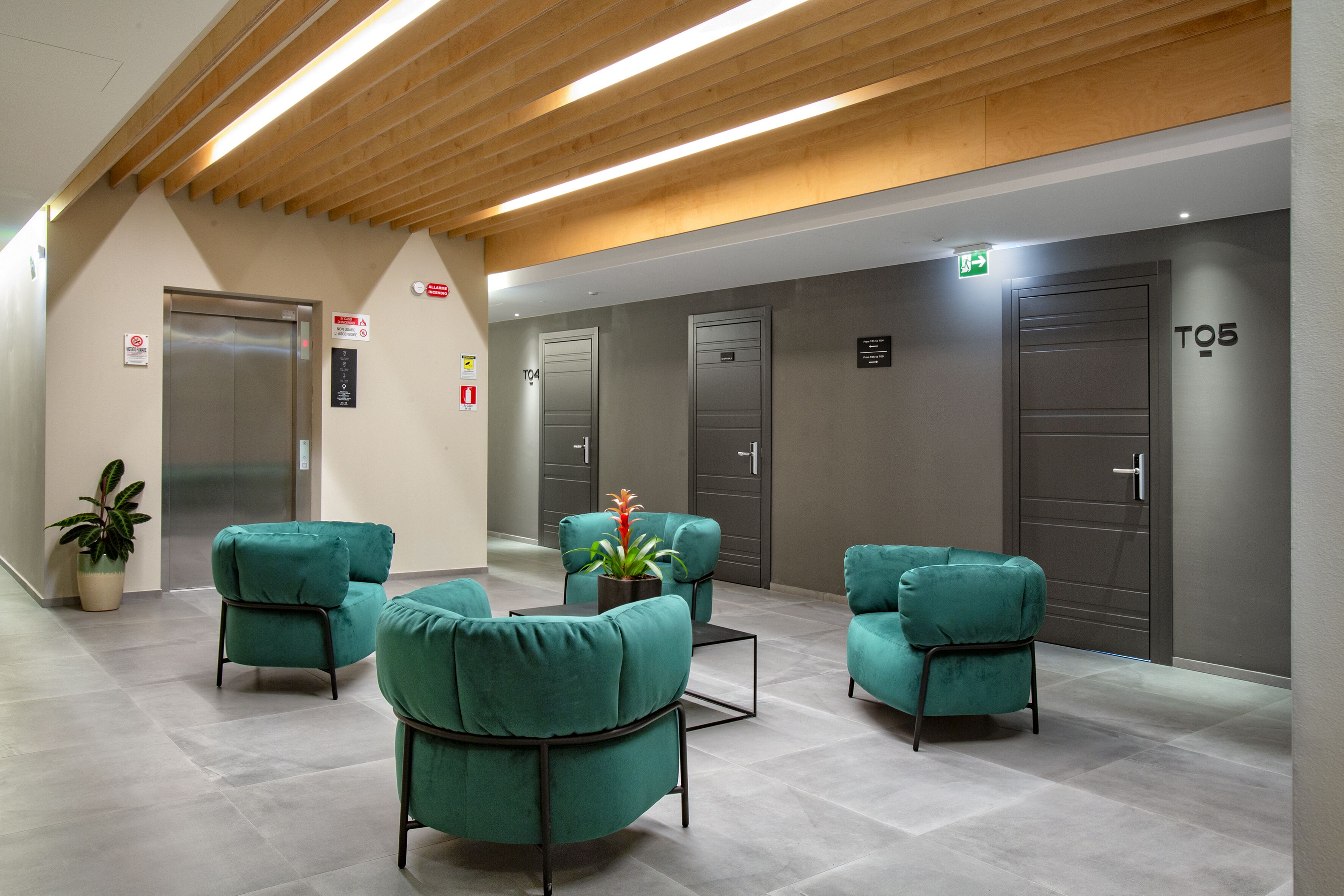 A modern lobby with teal chairs, a potted plant, and a sign indicating the location of the elevator.