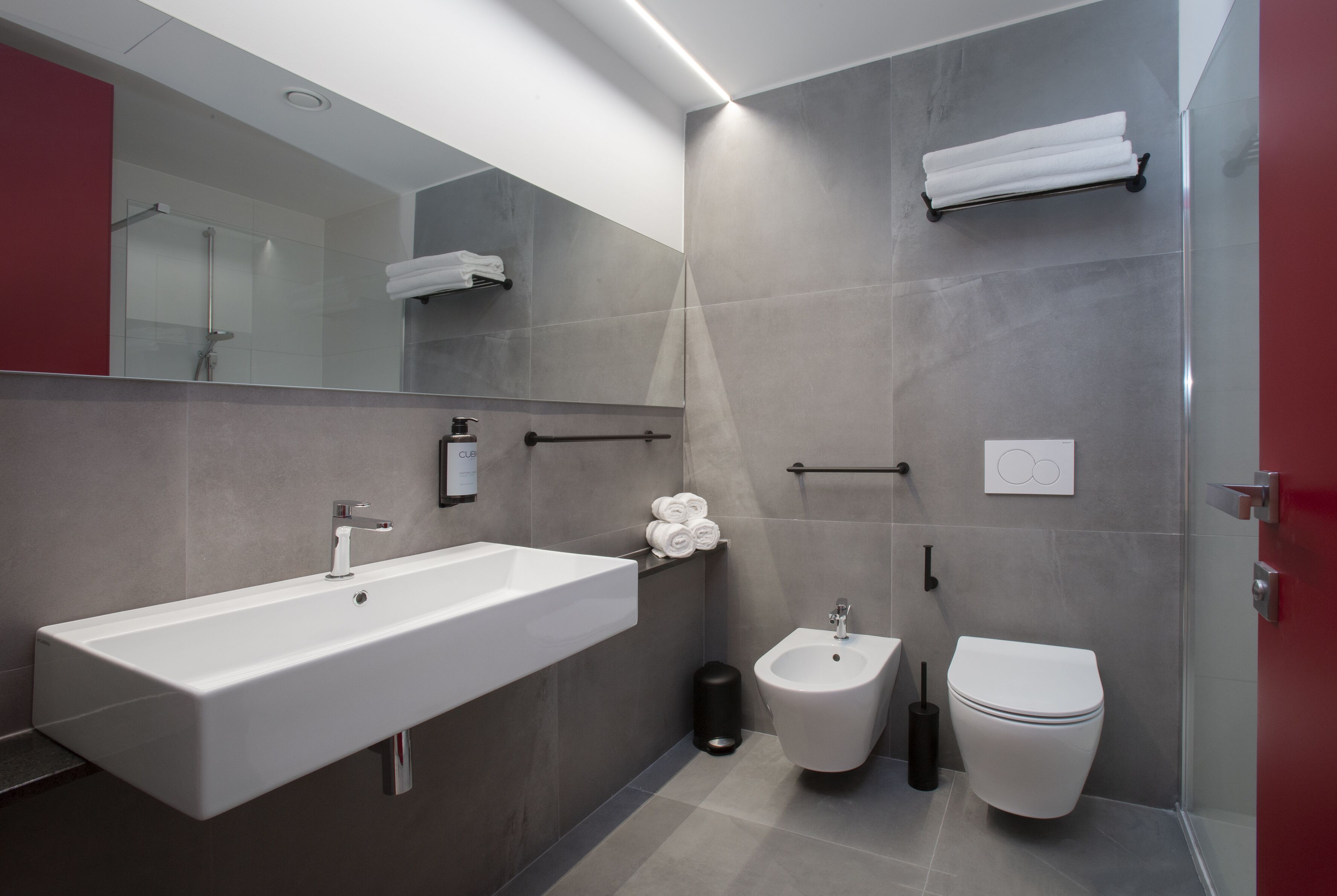 Ein modernes Badezimmer mit einem großen Waschbecken, einem Bidet, einer Toilette und einem Handtuchhalter.