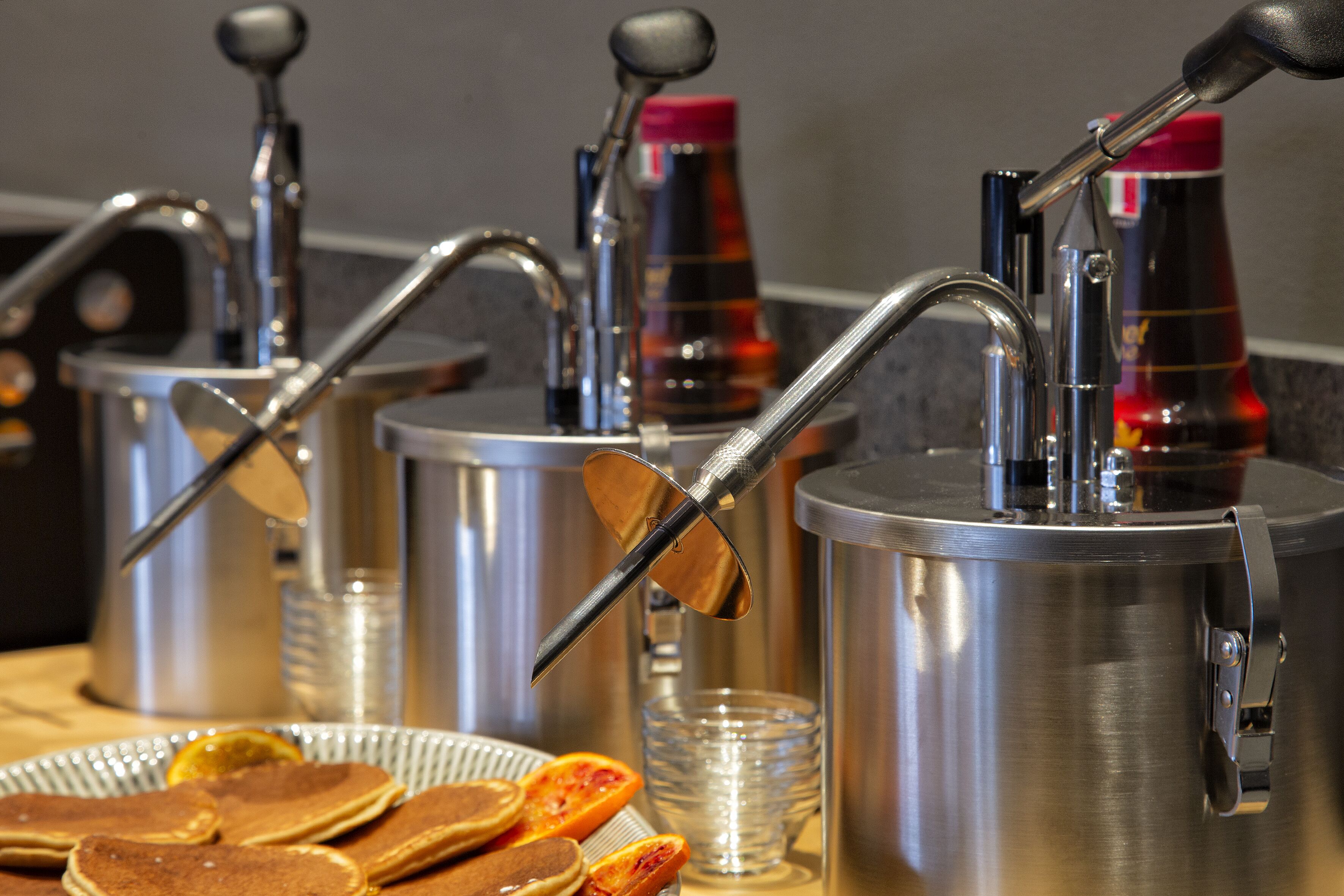 A breakfast setup with multiple coffee dispensers, a plate of pancakes, and a glass of orange juice.