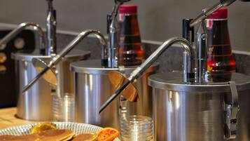 A breakfast setup with multiple coffee dispensers, a plate of pancakes, and a glass of orange juice.