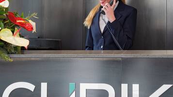 Ein Empfangsschalter mit einem Schild, auf dem 'CUBIK DESIGN RO' steht, und eine Frau am Telefon.