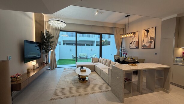 A modern living room with a sofa, a coffee table, a TV, and a dining area with chairs and a table. - Liva Suites By Hostiva - Dubai South (Dubai)