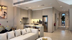 A modern kitchen with built-in appliances, a dining area with a sofa and table, and a living room with a coffee table. - Liva Suites By Hostiva - Dubai South (Dubai)