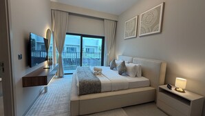A modern hotel room with a large bed, a TV, a bedside table with a lamp, and a view of the outside. - Liva Suites By Hostiva - Dubai South (Dubai)