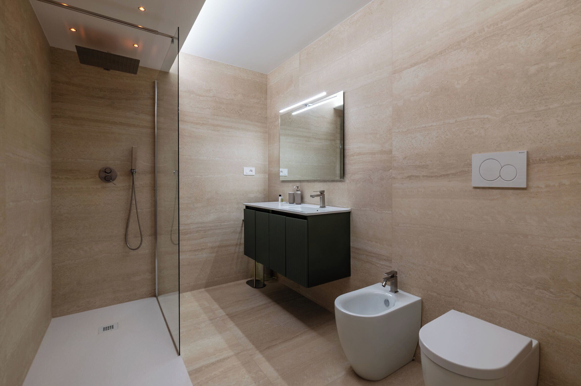 A modern bathroom with a glass shower enclosure, a dark-toned vanity, a bidet, and a toilet.