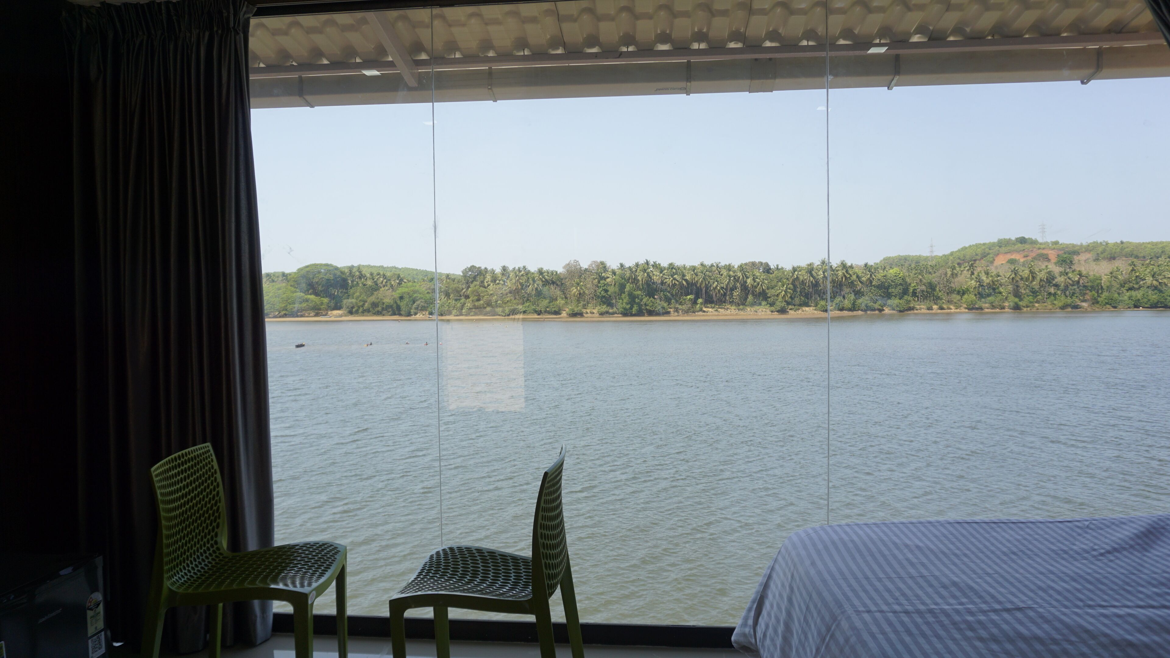 Une pièce dotée d’une grande fenêtre donnant sur un lac paisible, de deux fauteuils verts et d’un lit recouvert d’une couvre-lit à rayures.