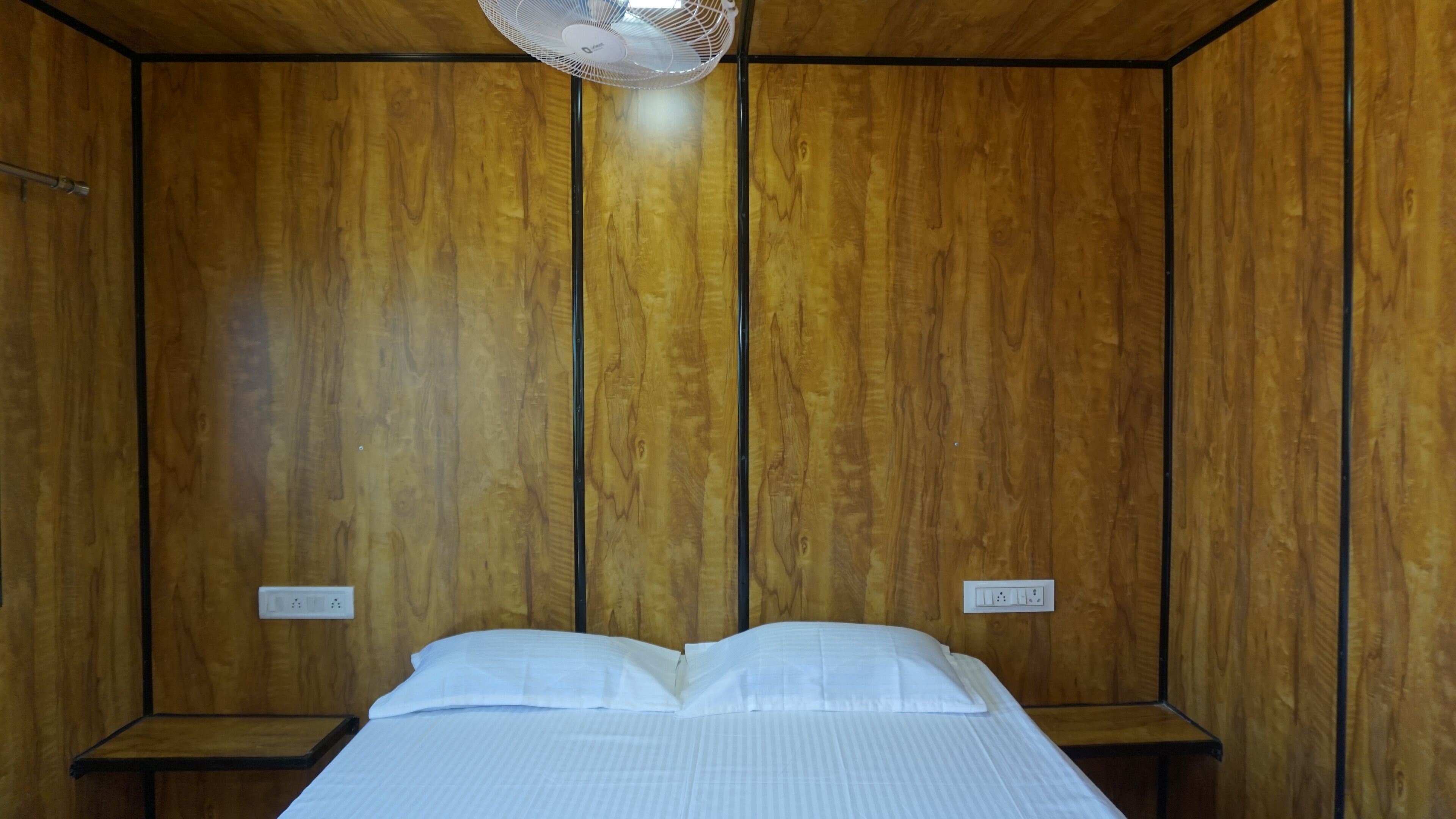 A room with wooden panel walls, a bed with white bedding, and a ceiling fan.