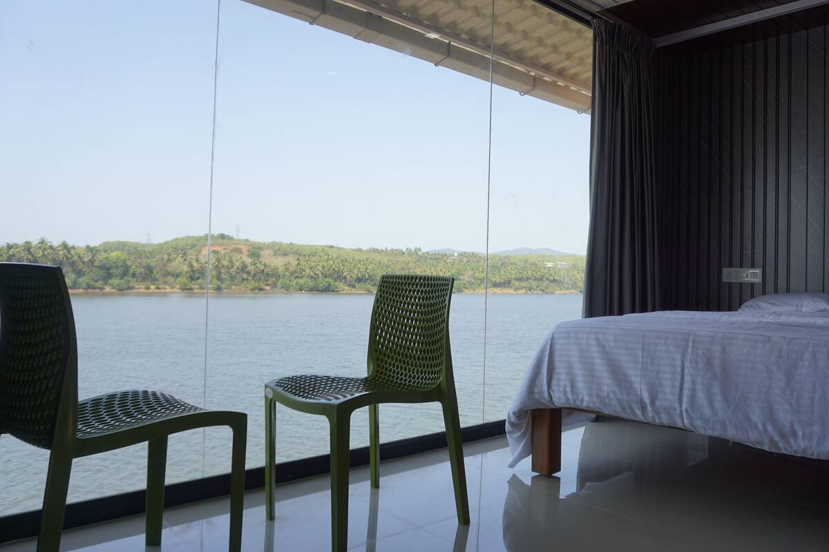 A room with a bed, two chairs, and a view of a lake.