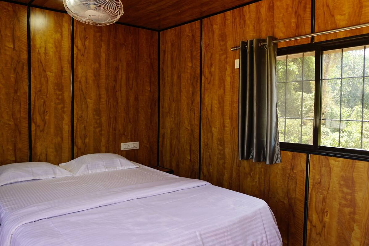A wooden-paneled room with a bed, a window with curtains, and a ceiling fan.