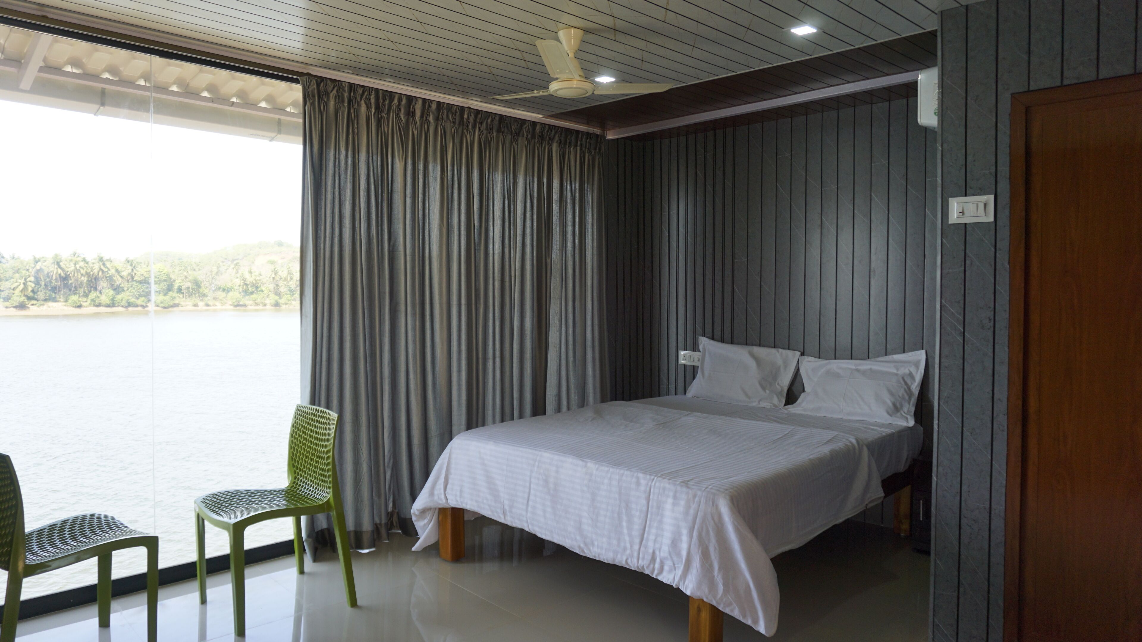 Un dormitorio con una cama, una silla, un ventilador de techo y vista a un lago.