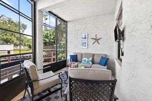 A sunlit room with a large window, a sofa, a chair, and a star decoration on the wall. - 2BRCondo In Palm Harbor With Pool! (Palm Harbor)