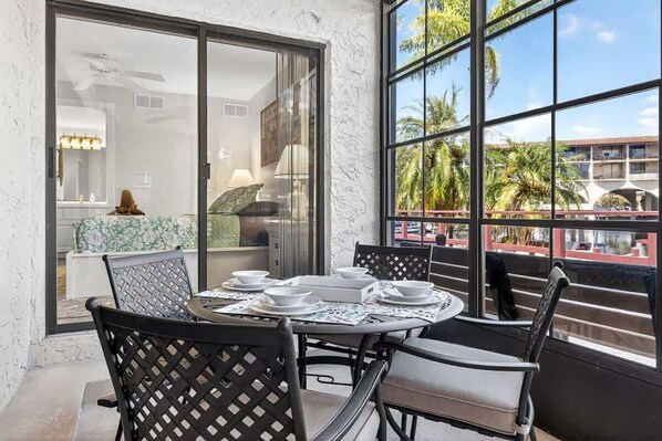 A dining area with a round table set for four, black chairs, and a view of a building with palm trees outside. - 2BRCondo In Palm Harbor With Pool! (Palm Harbor)