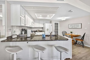 A modern kitchen with white cabinets, a granite countertop, and a bar area with stools. - 2BRCondo In Palm Harbor With Pool! (Palm Harbor)