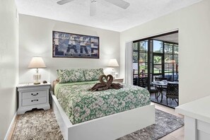 A bedroom with a bed, two bedside lamps, a framed picture on the wall, and a view through a glass door to an outdoor area. - 2BRCondo In Palm Harbor With Pool! (Palm Harbor)