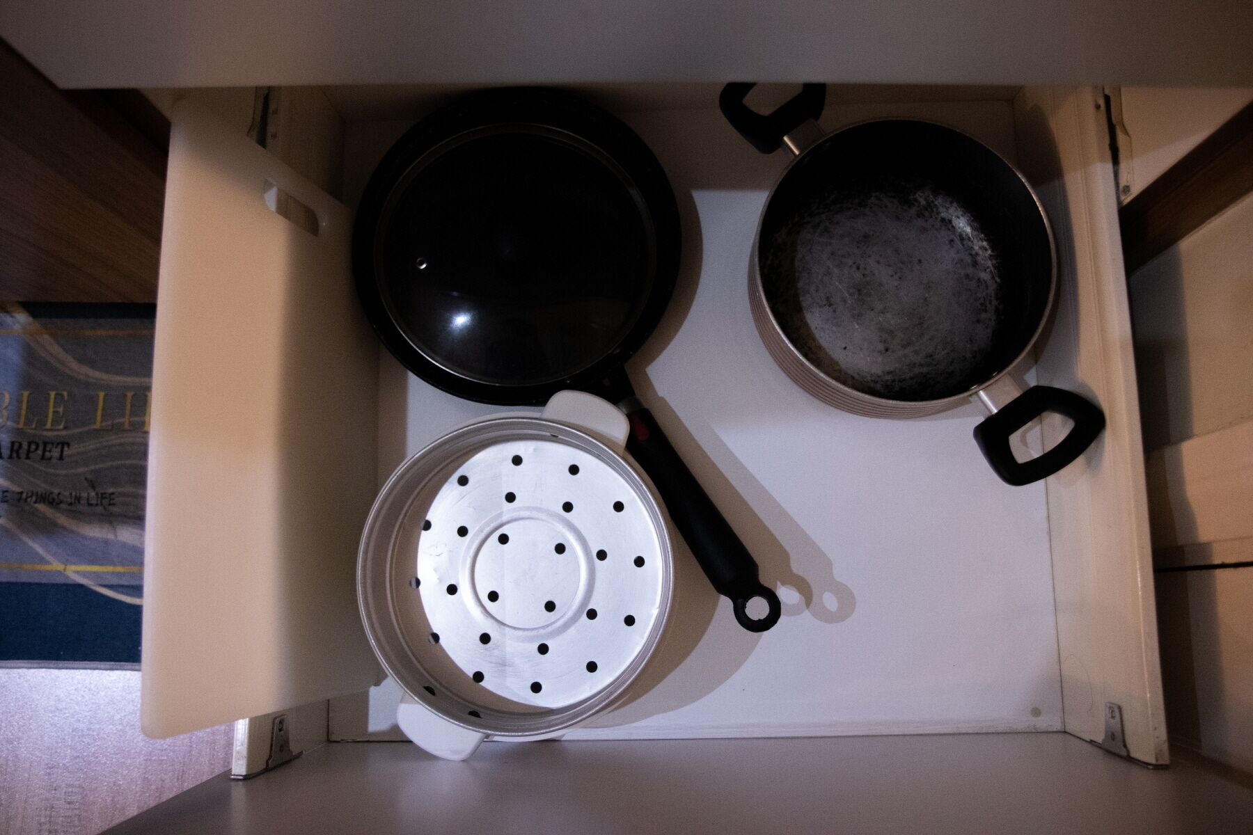 A kitchen with a white countertop, a black frying pan, a white colander, and a pan with a black handle.