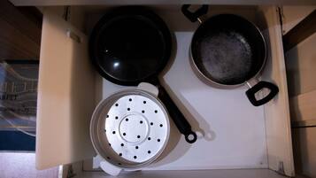 A kitchen with a white countertop, a black frying pan, a white colander, and a pan with a black handle.