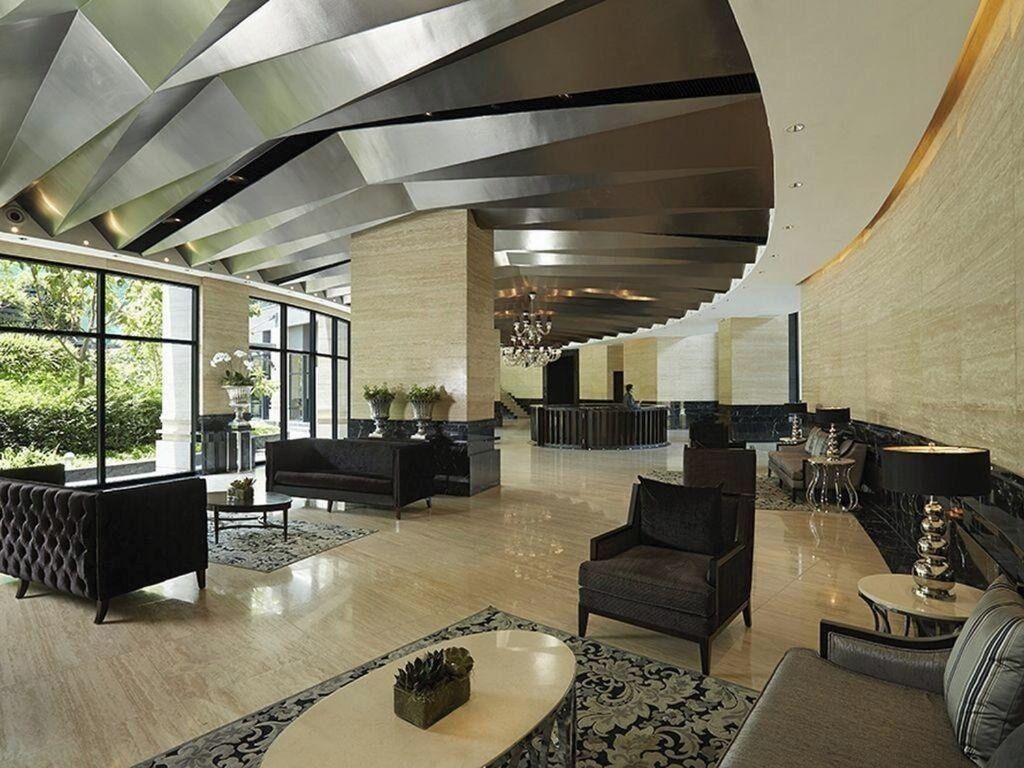 A spacious lobby with modern furniture, large windows, and a unique ceiling design.