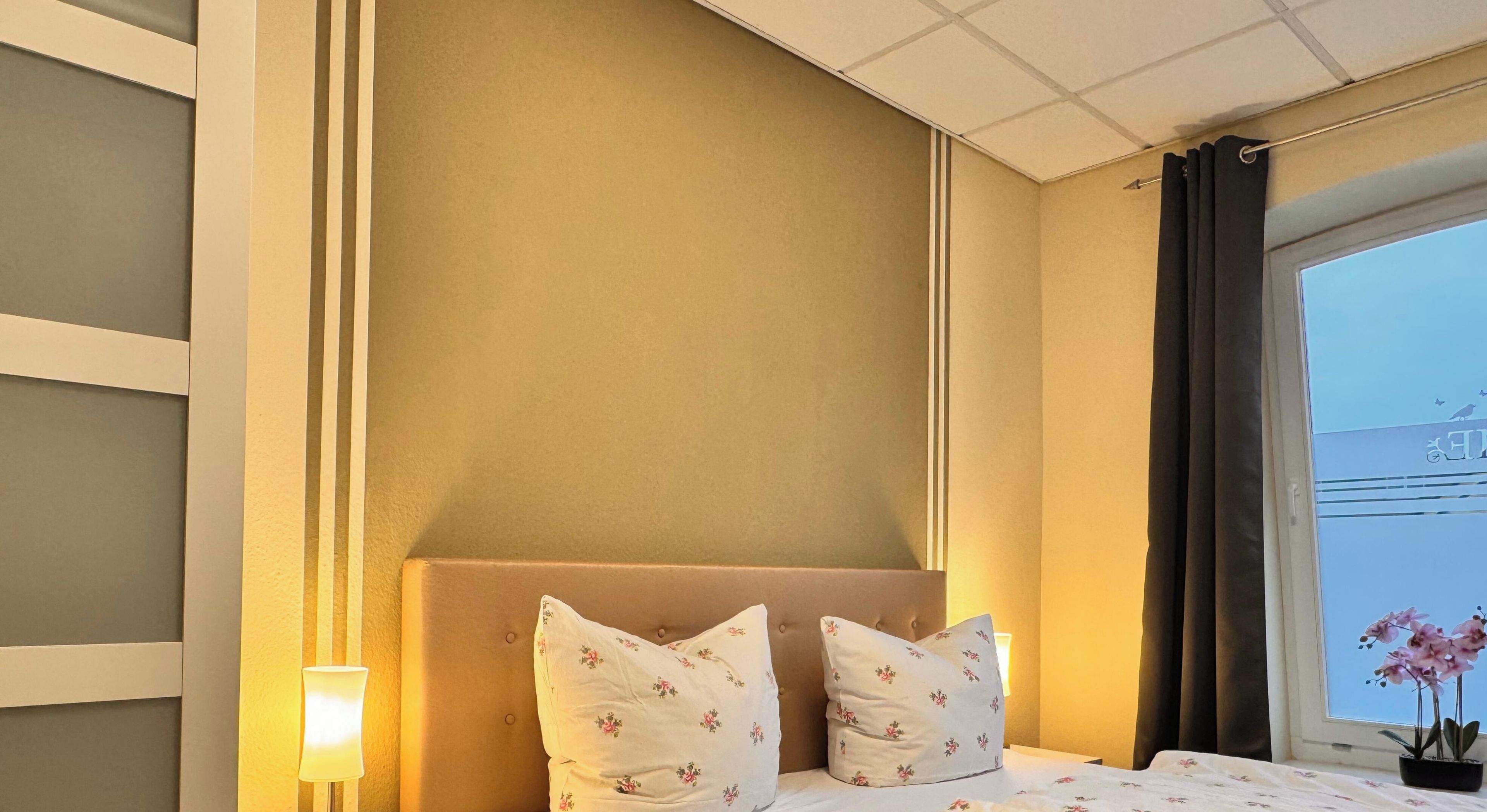 Une chambre d’hôtel avec un lit, une table de chevet, une lampe et une fenêtre avec des rideaux.