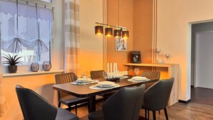 A dining area with a table set for four, chairs, a coffee machine, and a window with curtains. - Holiday Apartment "Auszeit Harz" – 3 Dogs Welcome, Fenced Garden, Private Guests Only (Bad Sachsa)