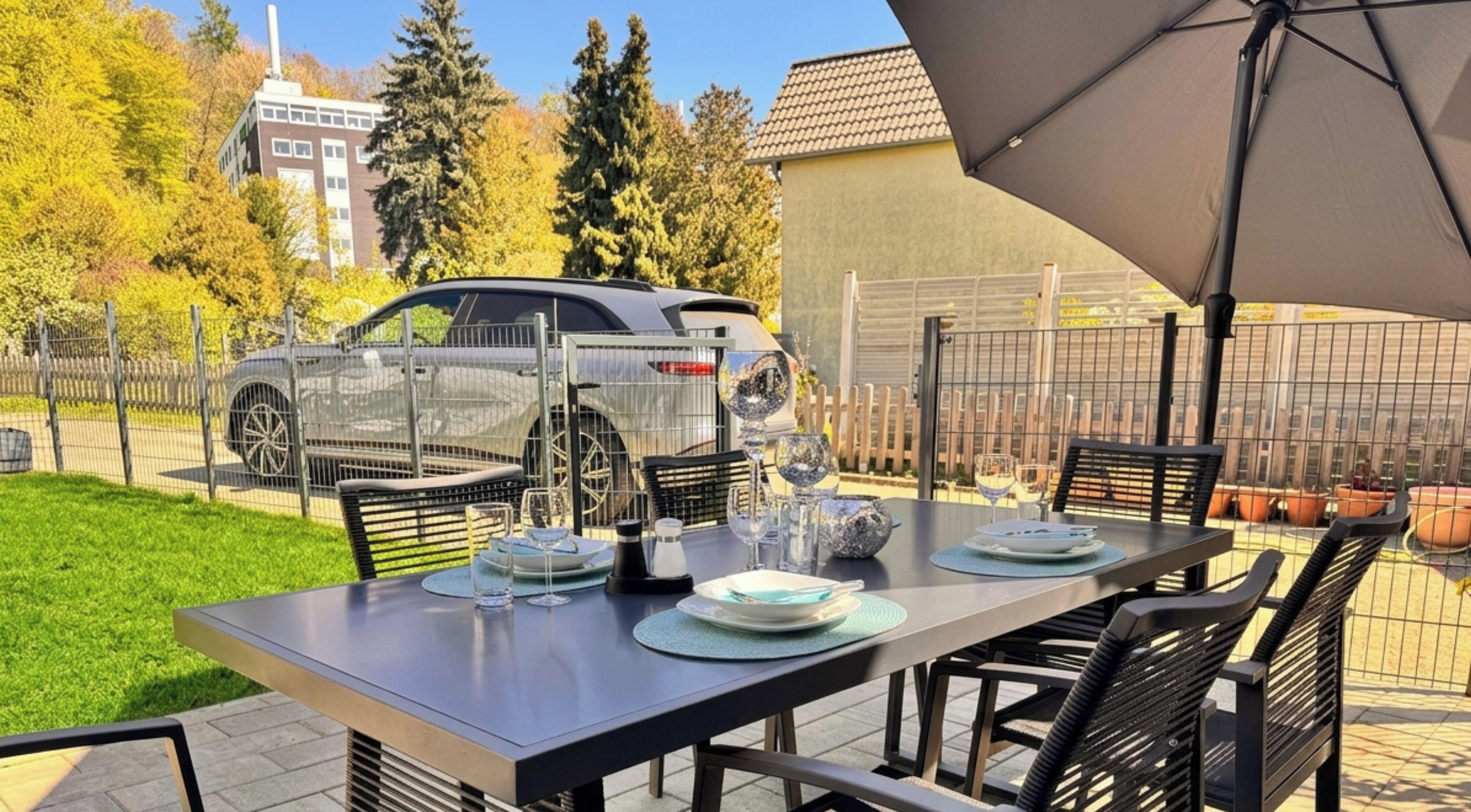 A terrace with a table set for dining, a car parked nearby, and a building in the background.