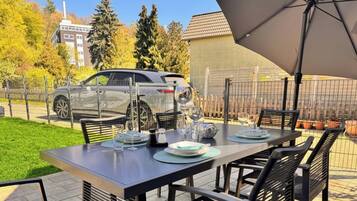 A terrace with a table set for dining, a car parked nearby, and a building in the background.